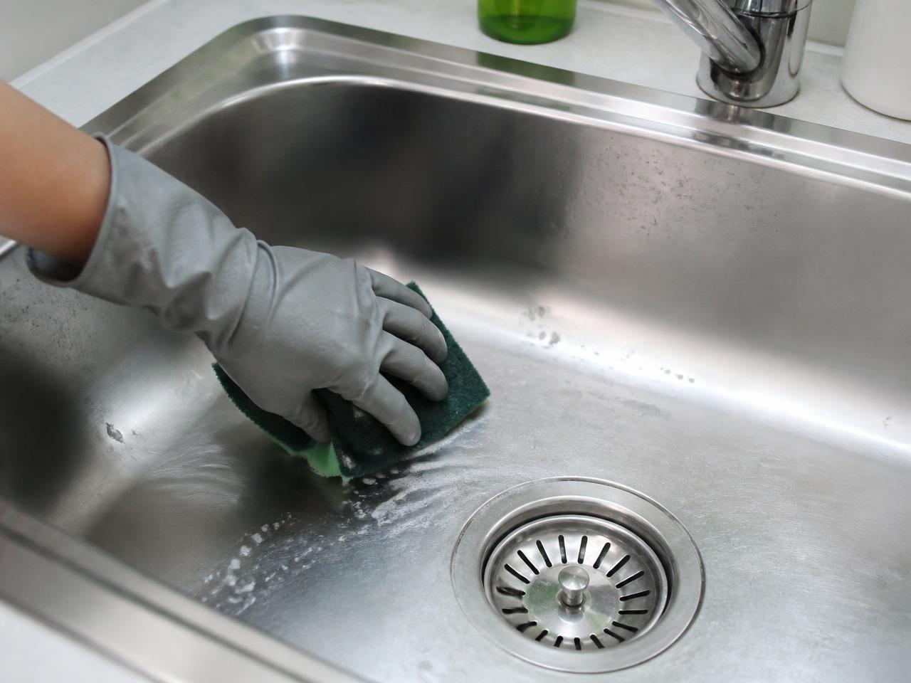 Gloved hand scrubbing a stainless steel kitchen sink